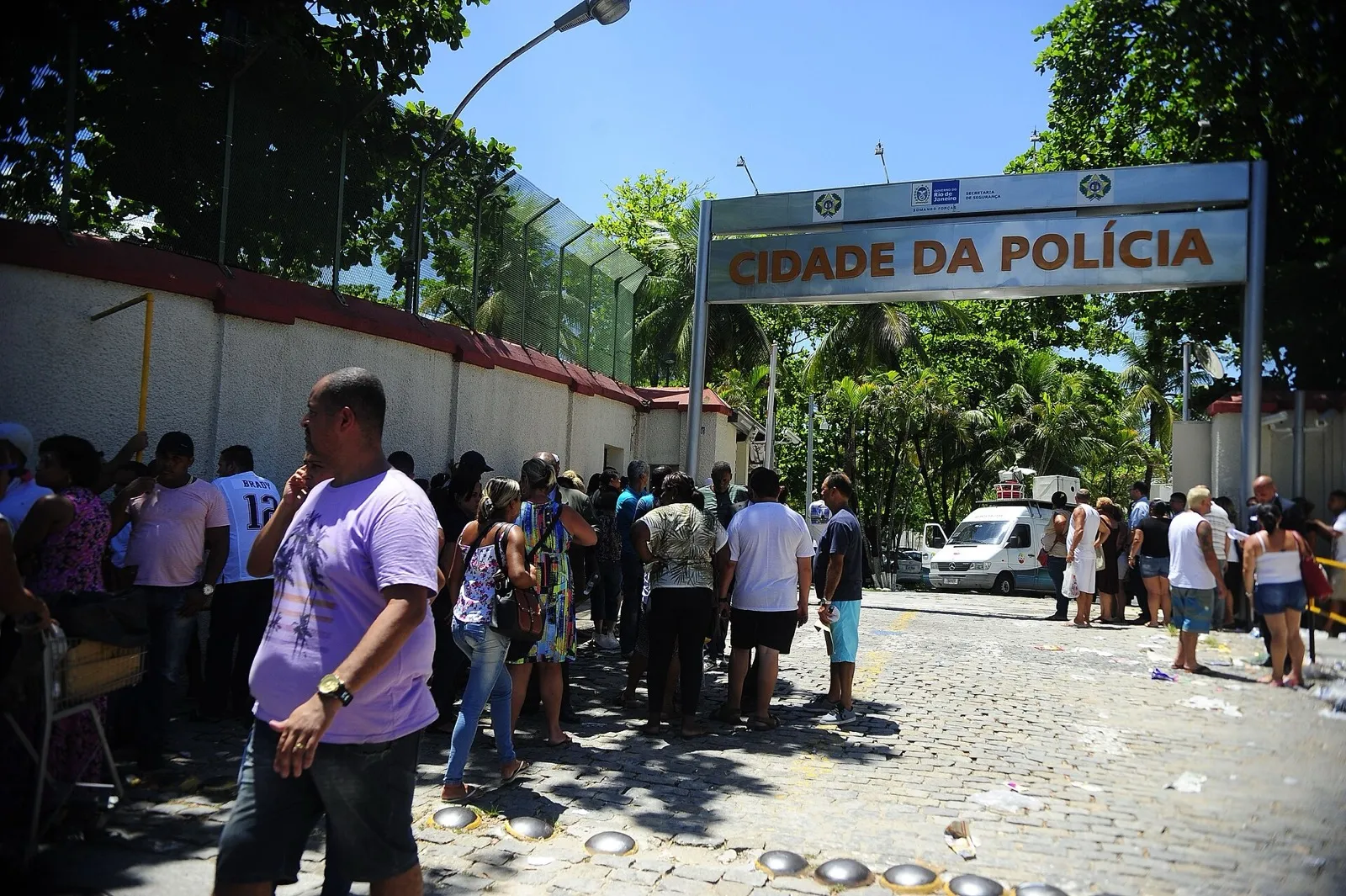 Pessoas em fila diante do portão de entrada da Cidade da Polícia, no Rio de Janeiro, sob um letreiro com o nome do complexo