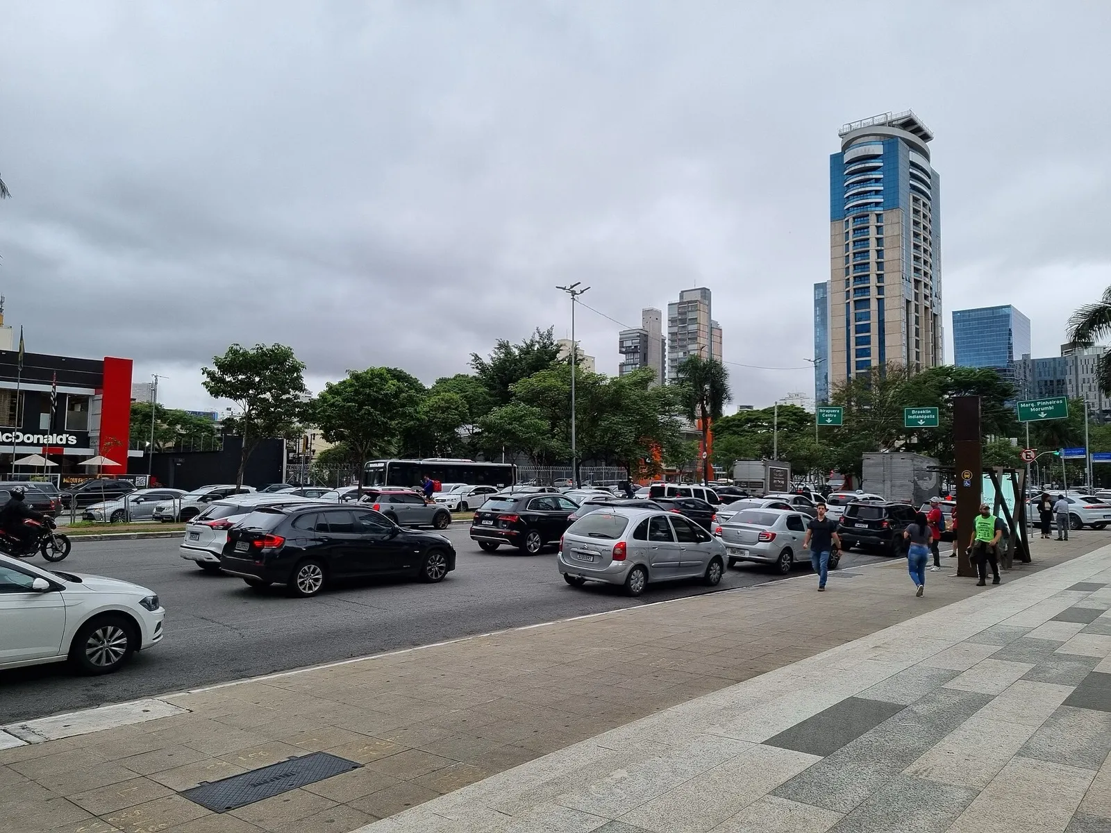 Trânsito intenso de carros na Avenida Faria Lima, em São Paulo, com prédios comerciais altos ao fundo sob céu nublado