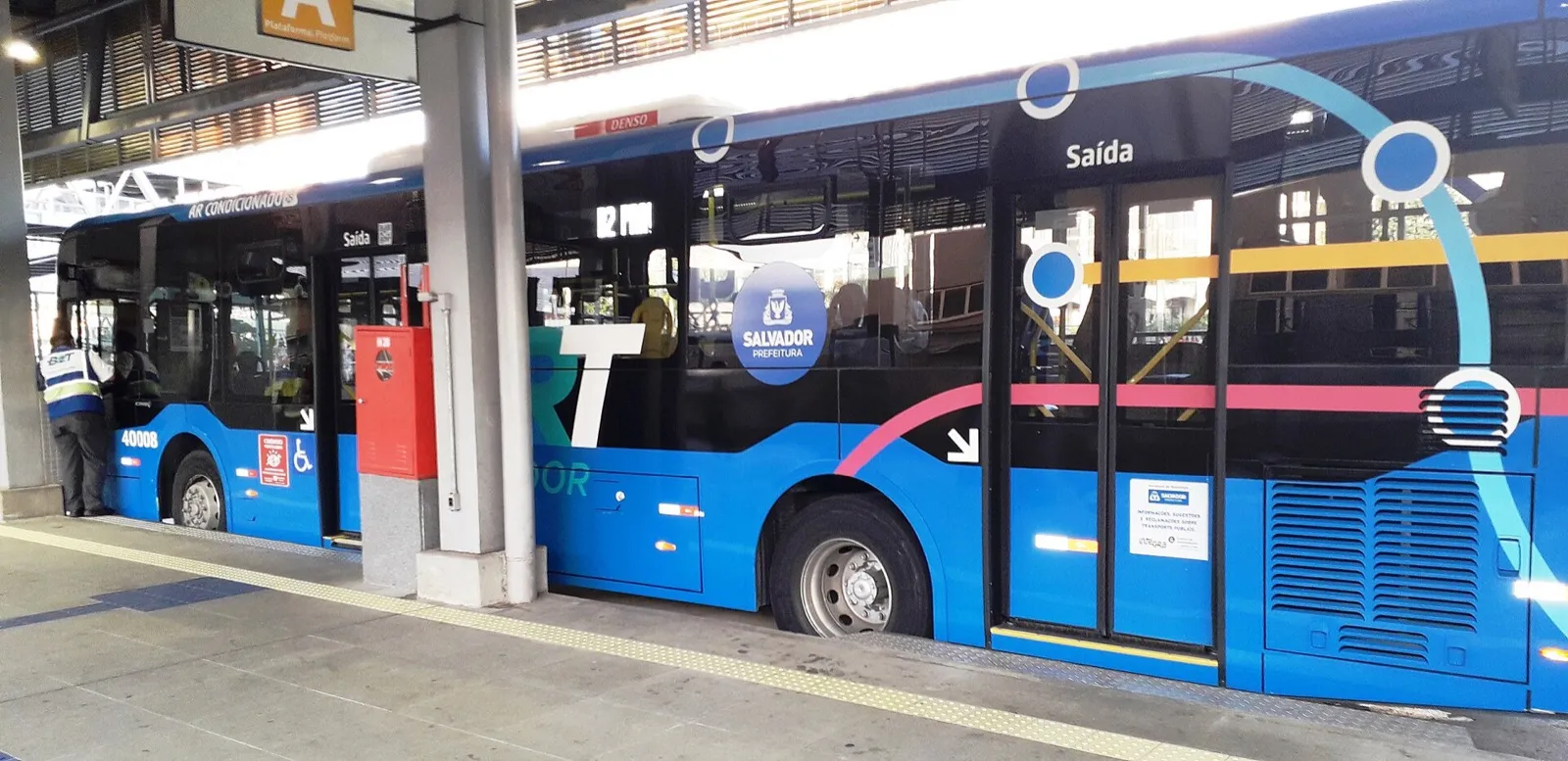 Ônibus azul do BRT de Salvador parado na estação, com a palavra Saída escrita sobre a porta e o brasão da prefeitura na lateral
